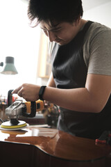 latin man shining the body of a guitar with a polishing machine in his repair shop