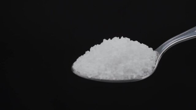 Pouring sea salt from an iron tablespoon on a black background close-up. For cooking food. In slow motion.