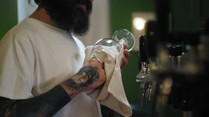 Barman standing behind bar counter and cleaning glass, barkeeper wiping beer mug close-up. Professional bartender working in restaurant. - Powered by Adobe