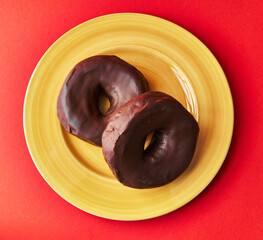  Plate of two chocolate doughnuts on a red background
