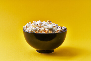 Fototapeta na wymiar Bowl of salty popcorns on a yellow background