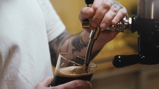 Barman pouring nitrogen beer into glass close-up. Bartender pours alcohol foamy drink in mug. Fresh beverage on bar counter background in pub.