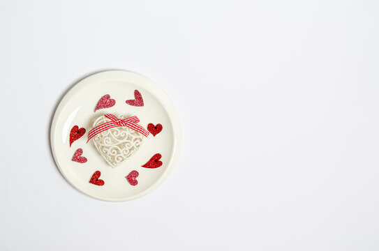 Heart in the form of a toy and different shiny hearts on a plate on a white background