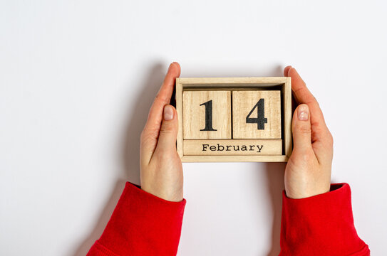 Wooden calendar with the date of February 14 in female hands on a white background
