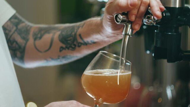 Barman pouring foamy beer in glass close-up. Alcohol golden drink, barkeeper pours frothy ale in mug. Fresh lager or pilsner, craft beer in pub. 