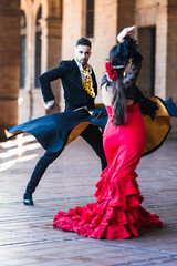 Man with a cape dancing flamenco with a woman in dress outdoors