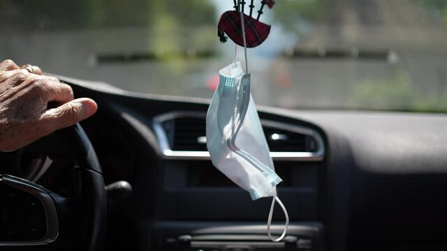 Surgical face mask hanging on rear-view mirror car interior