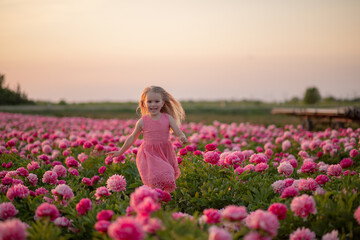 Obraz na płótnie Canvas cute little girl running on a peony field against a sunset background.