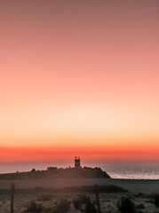 Fototapeta na wymiar Scenic Lighthouse And Pink Sky Sunset At The Beach In Nazareth Portugal