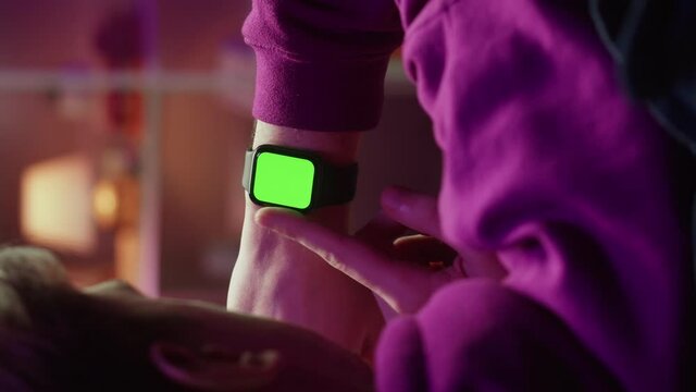 Vertical video of man using smartwatch with chroma key close-up. Young guy sitting on sofa and wearing fitness bracelet with green screen, back view.
