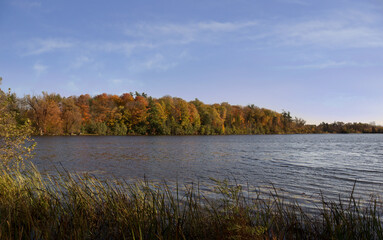 Beautiful autumn landscape view with Seneca lake surface reflecting blue sky and yellow orange red...