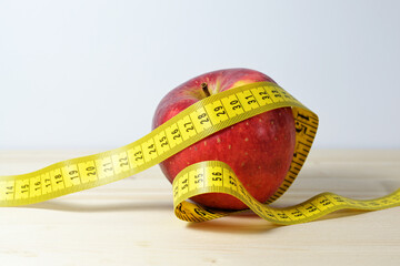 Red apple with a measuring tape, diet symbol for losing weight by healthy eating, light background with copy space, selected focus