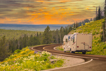 Camper Driving Down Road in The Beautiful Countryside Among Pine Trees and Flowers. - obrazy, fototapety, plakaty