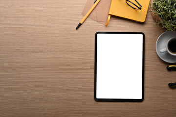 Above view digital tablet with blank screen, notebook and coffee cup on wooden table.