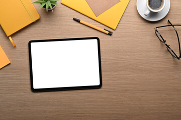Digital tablet with white screen and supplies on wooden table.