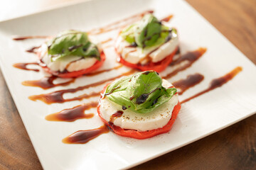 caprese salad - fresh tomato slices with mozzarella medalions and fresh basil on withe square plates with balsamic syrup