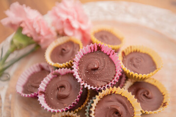 closeup homemade peanut butter cups in pastel wrappers and pink carnations