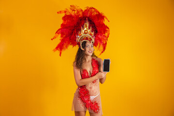 Beautiful young woman in special carnival feather costume holding a smartphone with blank screen...
