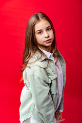 portrait of a beautiful girl in a green denim jacket and white shirt with loose hair. on a red background.