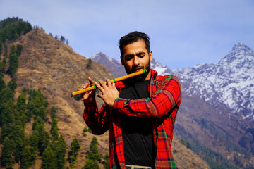 Young boy playing bansuri Indian flute in mountains