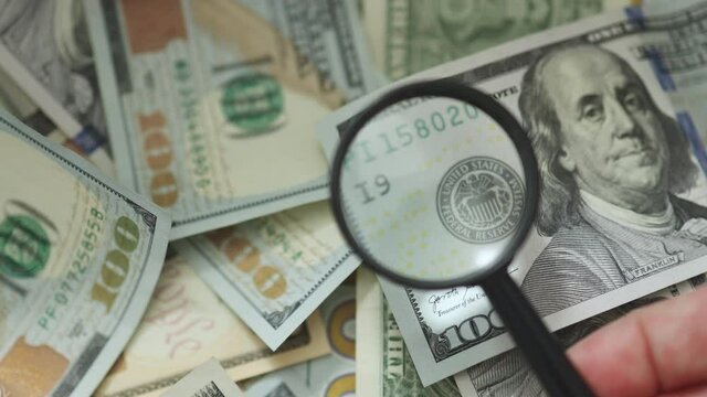 inspecting money with magnifying glass on hundred dollar bill. currency economy finance concept