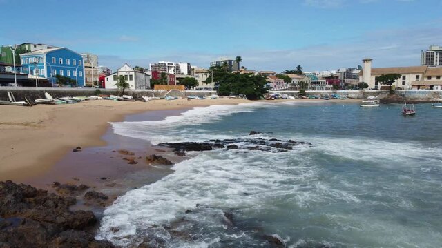 Aerial View near the sea of Salvador Coastline with waves, rocks and boats. Red River Beach in Salvador of Carnival state of Bahia Brazil. Tropical City Environment with cars passing by.
