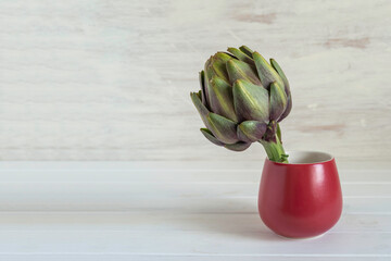 Fresh artichoke in red vase on white wooden background with copy space.