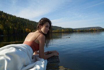 Fototapeta premium A young attractive woman of model appearance rests under a blanket on a pier. long hair. High quality photo