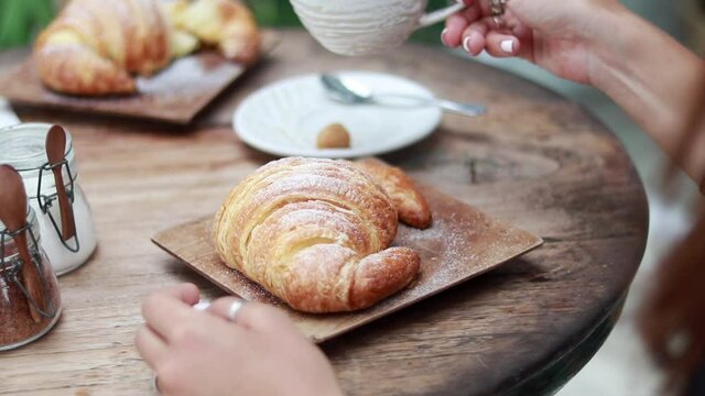 Young woman having delicious breakfast with coffee and croissant at table in cafe, closeup