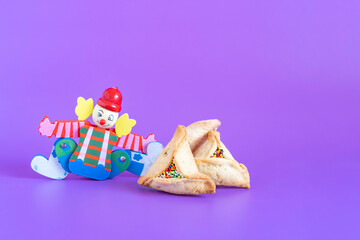 Decoration for Jewish holiday Purim. Traditional cookies Hamantashen and clown toy on purple background with copy space.
