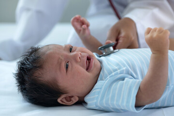 Obraz na płótnie Canvas Pediatric doctor exams newborn baby girl at home, doctor listens to the heart with a stethoscope