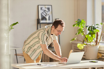 Horizontal medium shot of modern Caucasian man wearing eyeglasses standing at desk in modern office...