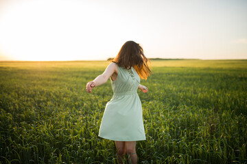 young, beautiful Asian girl in a field of green wheat on the background of the sunset