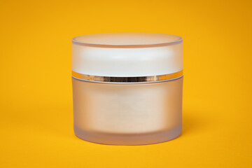 Jar of cream on yellow background. Blank packaging clear cosmetic cream