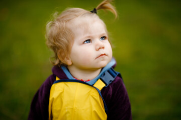 Cute adorable toddler girl playing outdoors on spring day. Baby child wearing yellow mud rain...