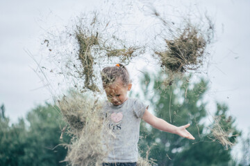 Defocused little girl 3-4 years old jumps and plays in hay stack, throwing it up. Creative motion blur - obrazy, fototapety, plakaty