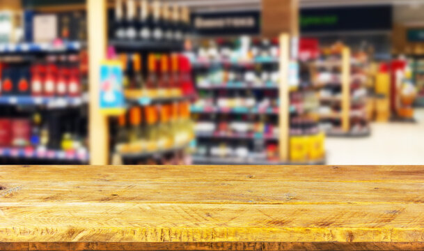 Empty wood table top on blurred market racks with bottles of alcoholic beverages. Mock up for display of product.