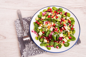On a white platter, fresh vegetable salad of spinach leaves, mozzarella cheese, avocado, pomegranate seeds, walnuts with lemon juice. Healthy vitamin food for a vegetarian. 