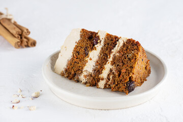 A piece of homemade carrot cake with cream, walnuts and cinnamon on a plate.