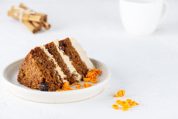 A piece of homemade carrot cake with cream, walnuts and cinnamon on a plate with a cup of tea.