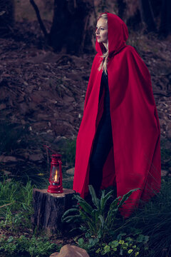 Attractive woman dressed a little red riding-hood walk in a dark forest with lantern