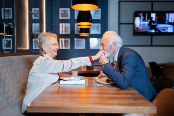 Elderly man kissing a hand of his partner during the romantic dinner in the restaurant