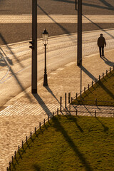 A vertical sunset street scene with an old man walking in the distance next to a cobbled street, on...