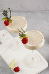 Cocktail glasses with sweet banana milk shake beverage, raspberries and coconut on white marble board