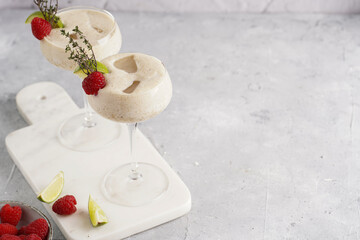 Cocktail glasses with sweet banana milk shake beverage, raspberries and coconut on white marble board