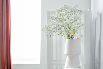Vase with gypsophila flowers on shelf near window
