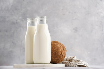 Two bottles with non-dairy milk and coconut on round marble board, grey background