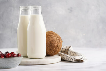 Two bottles with non-dairy milk, cranberries and coconut on round marble board, grey background