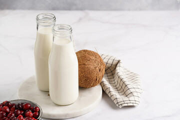 Two bottles with non-dairy milk, cranberries and coconut on round marble board, grey background