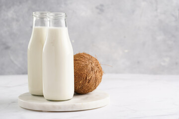 Two bottles with non-dairy milk and coconut on round marble board
